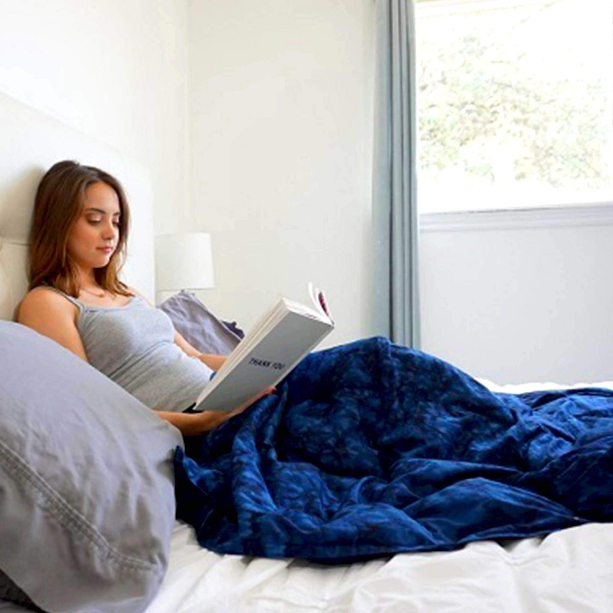 Woman reading in bed snuggled under her Mosaic Weighted Blankets Indigo Ocean Waves Weighted Blanket